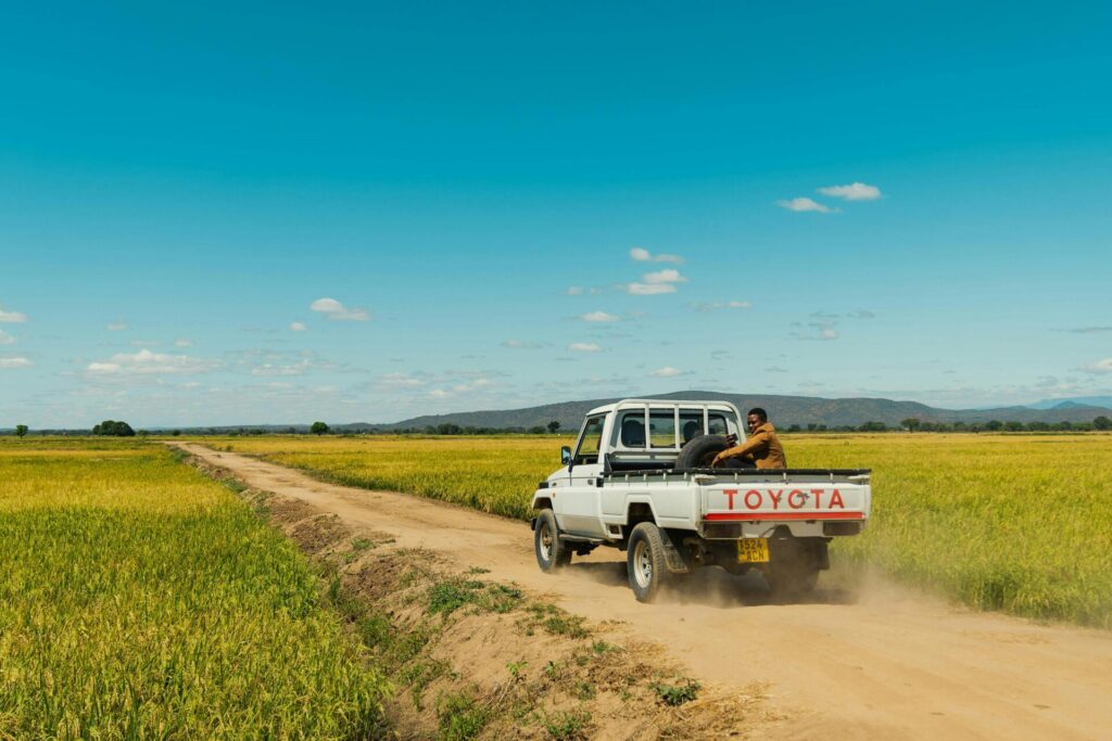 A truck drives along a dusty path through vast fields under a clear sky in Tanzania.